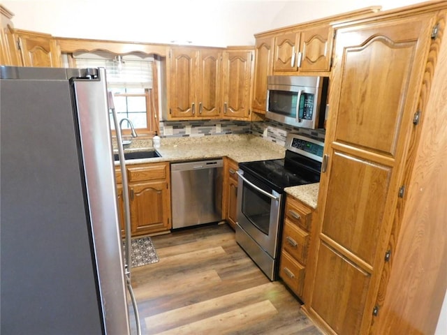 kitchen featuring sink, tasteful backsplash, appliances with stainless steel finishes, light stone countertops, and light hardwood / wood-style floors