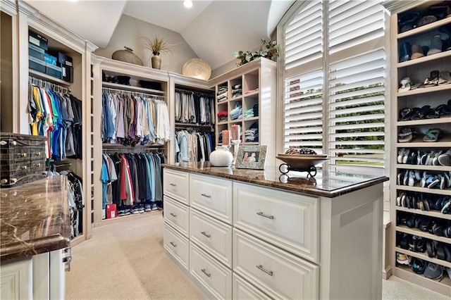 walk in closet with vaulted ceiling and light colored carpet