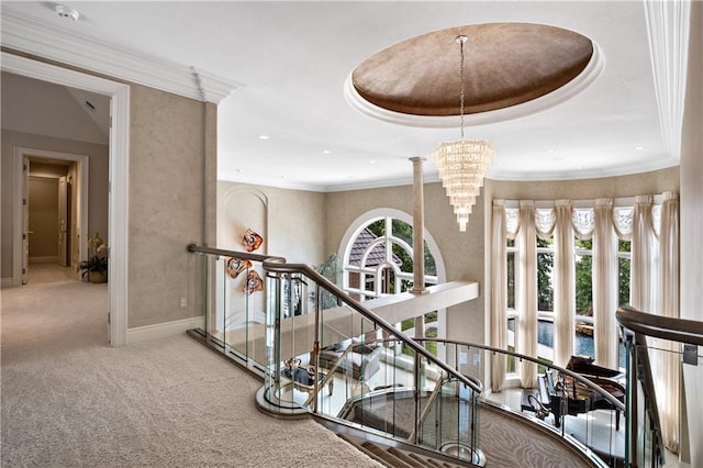 hall with a raised ceiling, crown molding, carpet floors, and an inviting chandelier