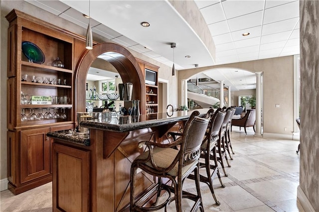 bar with light tile patterned flooring, dark stone counters, hanging light fixtures, and built in shelves