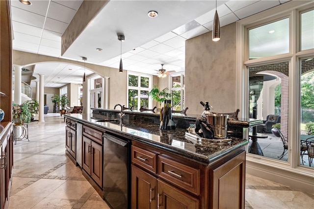 kitchen with black dishwasher, a sink, ceiling fan, ornate columns, and dark stone counters