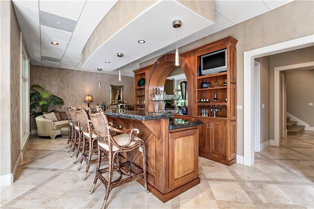 bar featuring dark stone counters, decorative light fixtures, light tile patterned floors, and a paneled ceiling