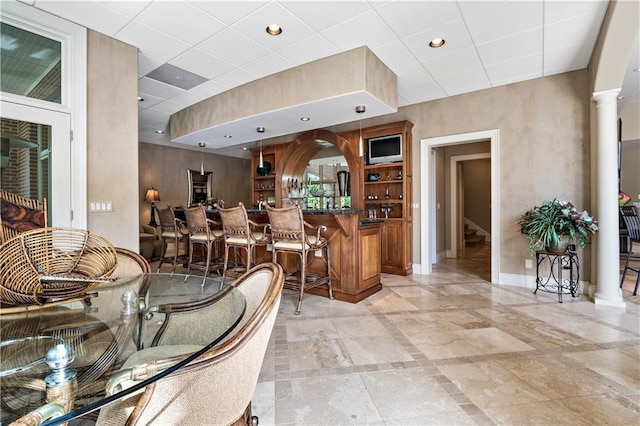 interior space featuring baseboards, recessed lighting, a community bar, stairs, and decorative columns