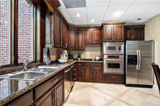 kitchen with light tile patterned floors, dark stone counters, appliances with stainless steel finishes, dark brown cabinetry, and sink