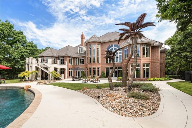 back of property with stairway, a patio, brick siding, and an outdoor pool