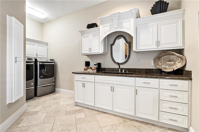 clothes washing area featuring cabinet space, stone tile floors, a sink, baseboards, and washing machine and dryer