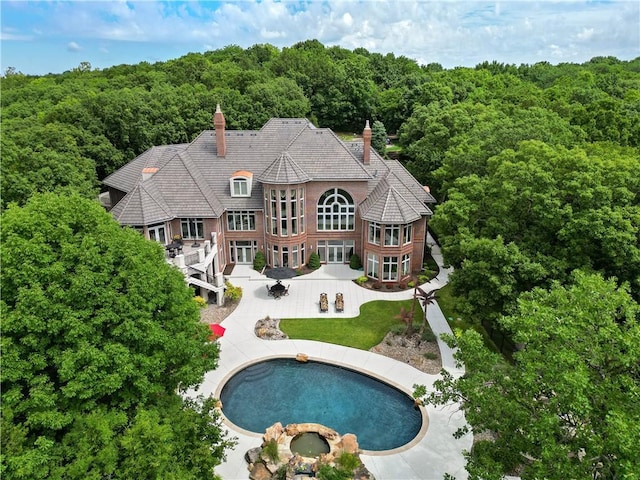 rear view of property with a wooded view, a patio, an in ground hot tub, and a chimney