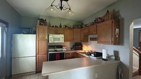 kitchen with white microwave, range, light tile patterned floors, kitchen peninsula, and stainless steel fridge