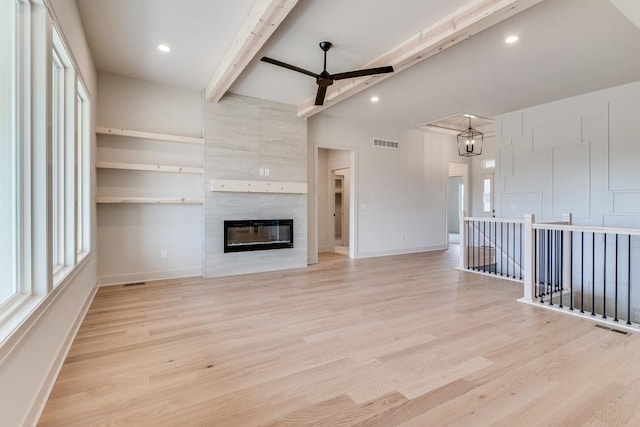 unfurnished living room with ceiling fan, a fireplace, beamed ceiling, and light hardwood / wood-style floors