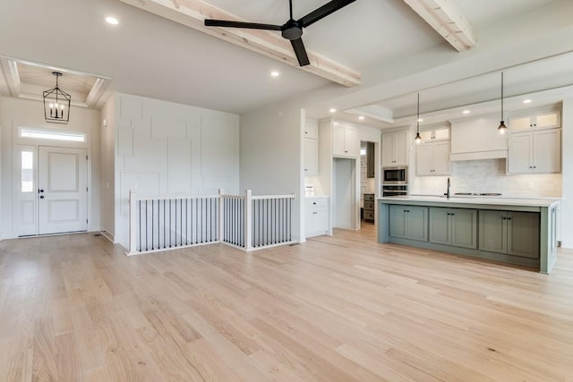 kitchen with a kitchen island with sink, stainless steel microwave, pendant lighting, and light hardwood / wood-style floors