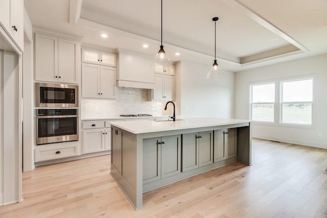 kitchen with white cabinets, stainless steel appliances, a kitchen island with sink, and a tray ceiling