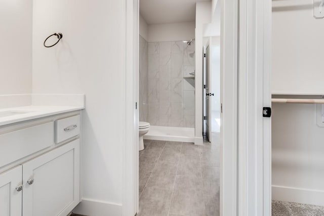 bathroom featuring toilet, a tile shower, vanity, and tile patterned floors