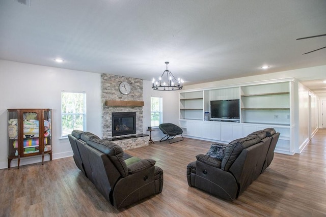 living room featuring a notable chandelier, built in features, wood-type flooring, and a stone fireplace