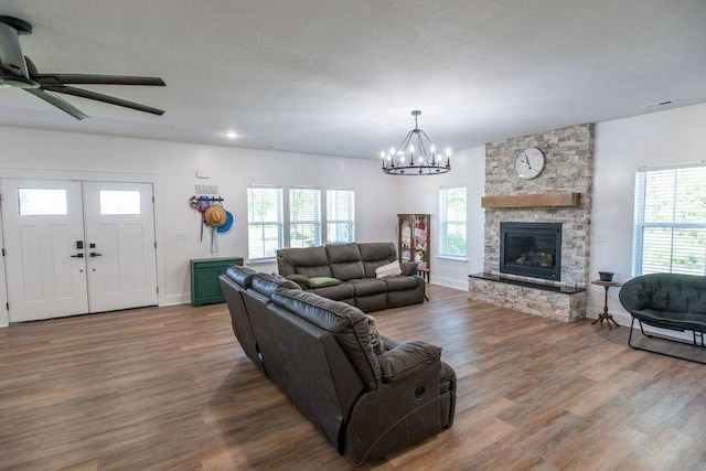 living room with ceiling fan with notable chandelier, hardwood / wood-style floors, a fireplace, and a textured ceiling