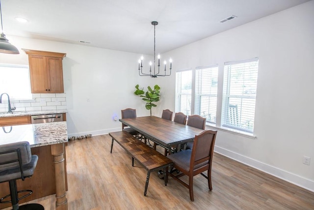 dining space with sink, light hardwood / wood-style flooring, and a notable chandelier