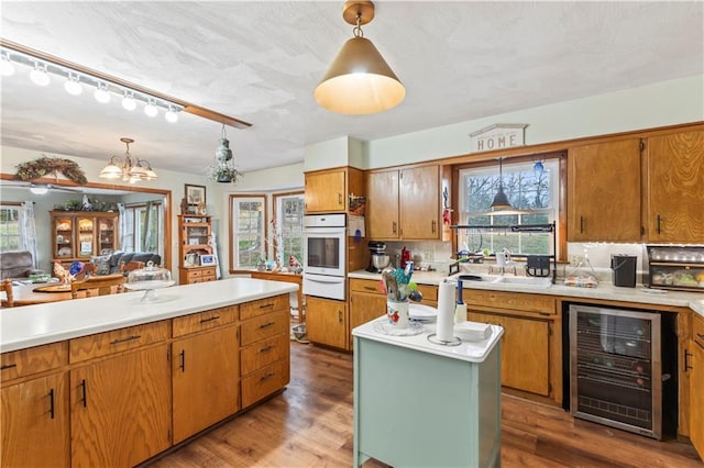 kitchen with beverage cooler, hardwood / wood-style floors, oven, a chandelier, and pendant lighting