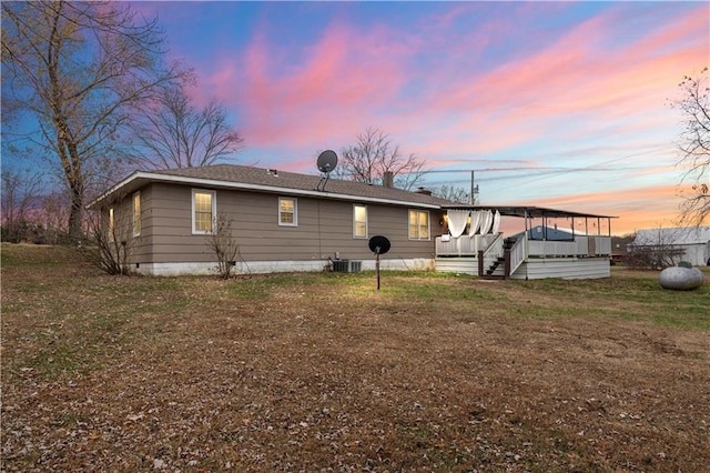 back house at dusk with central air condition unit and a yard