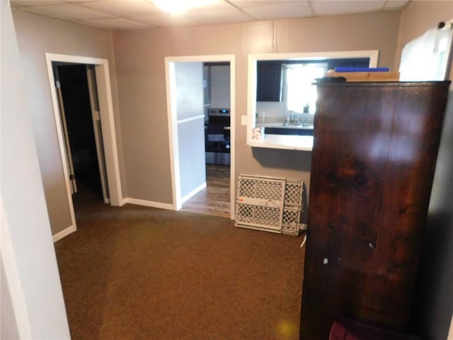 hall with sink, a drop ceiling, and dark carpet