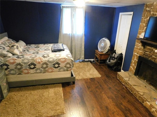 bedroom featuring a stone fireplace, dark wood-type flooring, and a closet