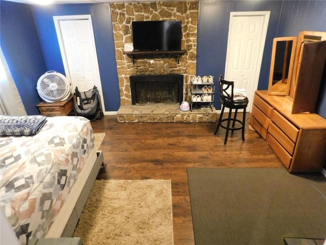 bedroom with dark hardwood / wood-style floors and a stone fireplace