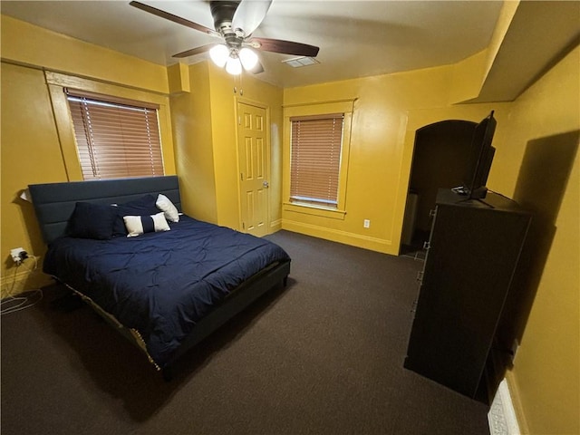 bedroom featuring a ceiling fan, baseboards, visible vents, arched walkways, and dark carpet