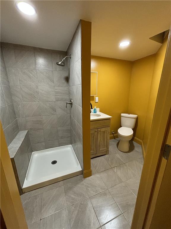 bathroom featuring tile patterned floors, toilet, a tile shower, baseboards, and vanity