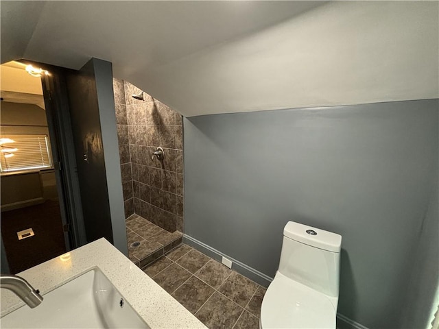 bathroom with baseboards, a tile shower, a sink, vaulted ceiling, and toilet