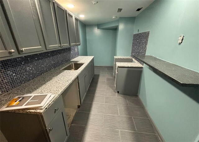 kitchen featuring baseboards, visible vents, gray cabinets, a sink, and decorative backsplash