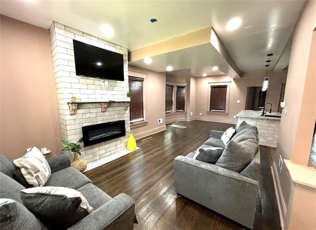 living room with brick wall, dark hardwood / wood-style flooring, a brick fireplace, and sink