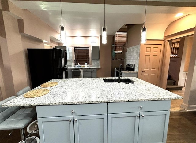 kitchen featuring light stone counters, freestanding refrigerator, a sink, stainless steel dishwasher, and tasteful backsplash