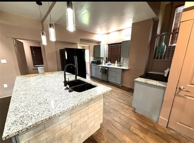 kitchen featuring light wood finished floors, dishwasher, gray cabinets, freestanding refrigerator, and a sink