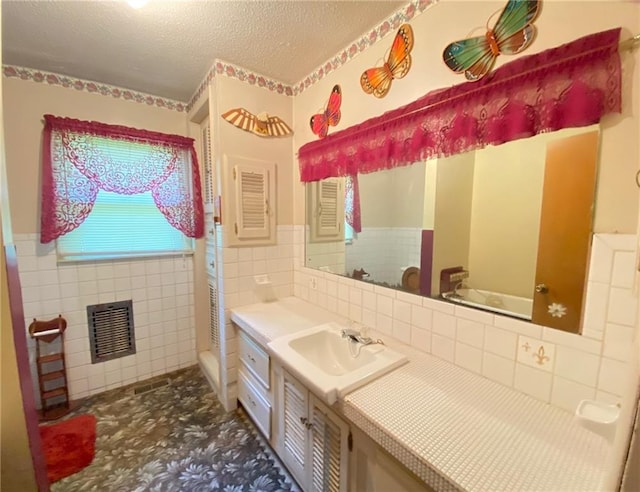 bathroom with visible vents, a textured ceiling, tile walls, and vanity