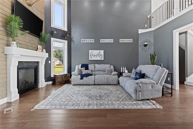 living room featuring wooden walls, dark wood-type flooring, a towering ceiling, and a premium fireplace