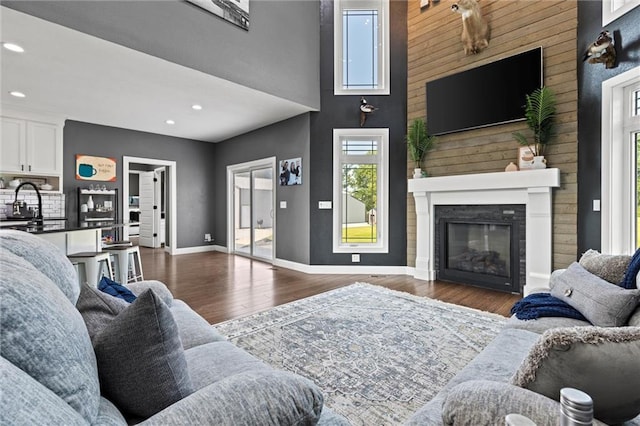 living room with hardwood / wood-style flooring, wooden walls, sink, and a high ceiling