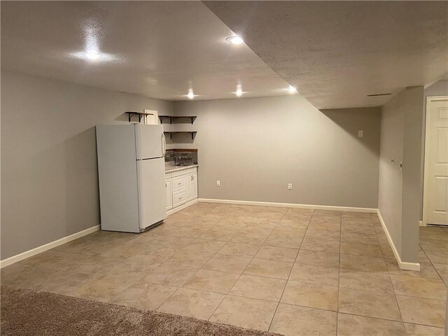 finished below grade area featuring freestanding refrigerator, a textured ceiling, baseboards, and light tile patterned floors