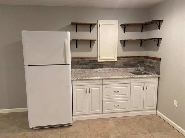 kitchen with freestanding refrigerator, a sink, light stone countertops, white cabinetry, and backsplash