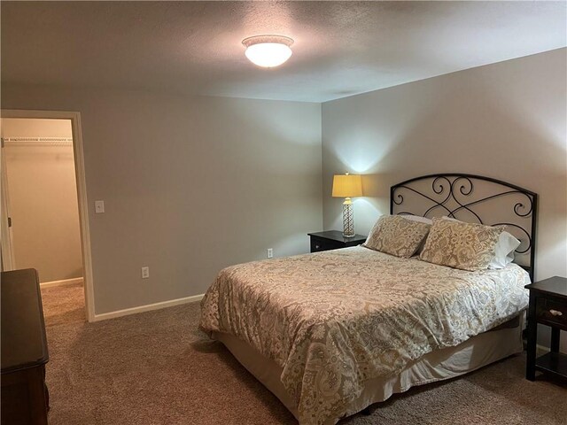 bedroom featuring a walk in closet, dark carpet, a textured ceiling, and baseboards