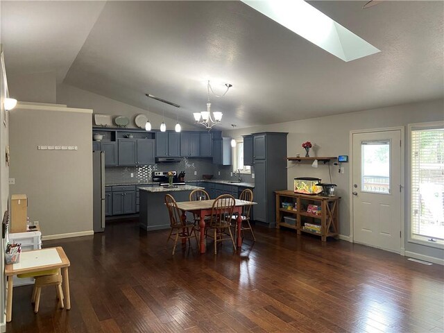 dining area with lofted ceiling with skylight, a chandelier, baseboards, and dark wood-style floors