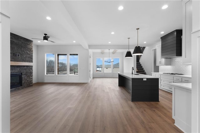 kitchen featuring a stone fireplace, sink, white cabinetry, a kitchen island with sink, and backsplash