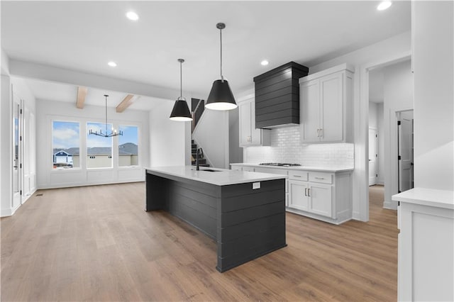 kitchen with white cabinets, backsplash, hanging light fixtures, a kitchen island with sink, and gas cooktop