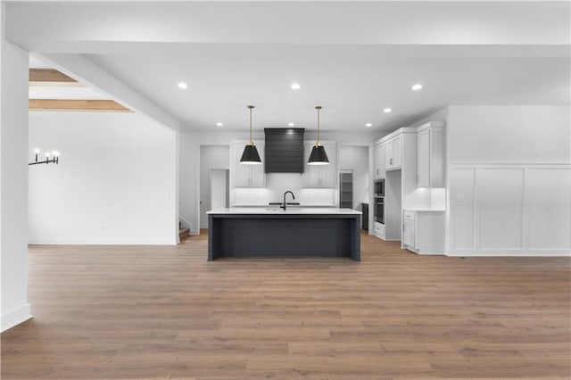 kitchen with hanging light fixtures, white cabinets, a center island with sink, decorative backsplash, and light wood-type flooring