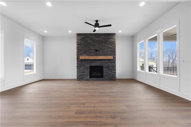 unfurnished living room with a stone fireplace, wood-type flooring, and ceiling fan