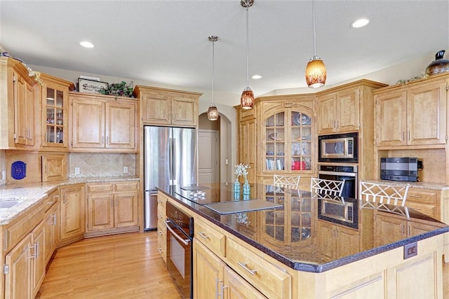 kitchen featuring dark stone countertops, decorative light fixtures, a center island, and black appliances