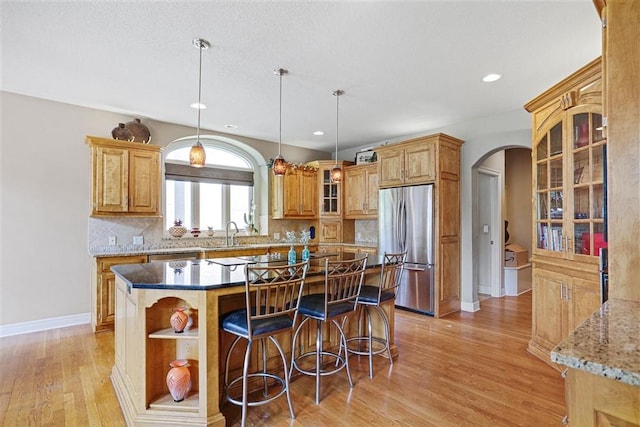 kitchen with a kitchen island, dark stone countertops, backsplash, stainless steel fridge, and light hardwood / wood-style floors