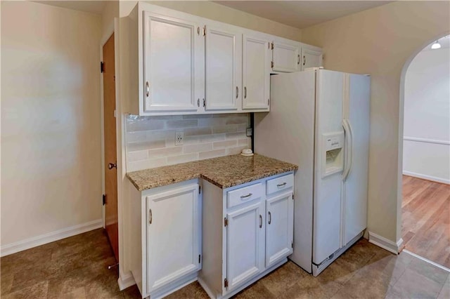 kitchen featuring hardwood / wood-style flooring, light stone counters, white cabinetry, white fridge with ice dispenser, and tasteful backsplash