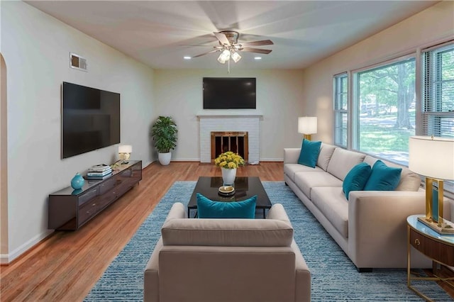 living room with a fireplace, wood-type flooring, and ceiling fan