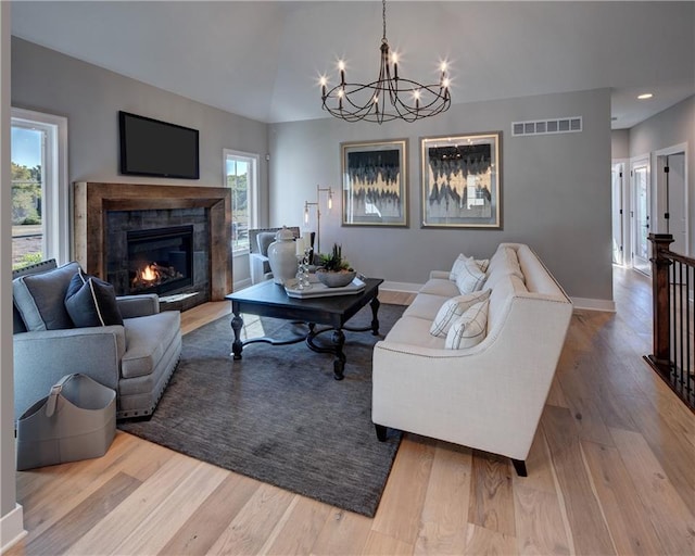 living room featuring a notable chandelier, a tile fireplace, a healthy amount of sunlight, and hardwood / wood-style floors