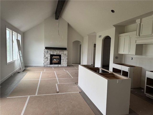 kitchen featuring visible vents, arched walkways, a fireplace, high vaulted ceiling, and beamed ceiling