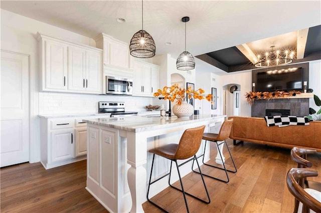 kitchen with appliances with stainless steel finishes, wood-type flooring, a kitchen breakfast bar, white cabinetry, and decorative backsplash