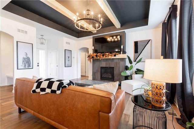 living area featuring visible vents, arched walkways, wood finished floors, a chandelier, and a glass covered fireplace
